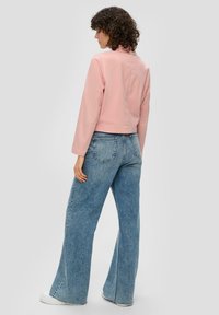 Rosa, gekürzte Jacke mit langen Ärmeln, kombiniert mit hochgeschnittenen, weit geschnittenen blauen Jeans aus Denim, die eine leichte Ausbleichung und gespaltene Säume aufweisen.