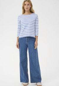 Bluză cu mâneci lungi cu dungi în albastru deschis și alb, asortată cu blugi evazați albaștri. Țesătură moale, croială lejeră și decolteu rotund simplu.