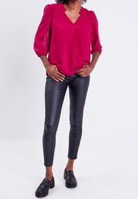 Blusa magenta con mangas transparentes de puntos, diseño de escote en V, combinada con leggings negros brillantes y mocasines negros. Textura suave y corte ajustado.