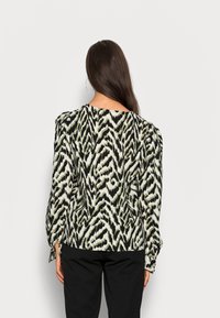 Camisa de mangas longas em padrão zebra preto e verde, com um caimento descontraído e mangas bufantes. Tecido suave com uma textura macia.