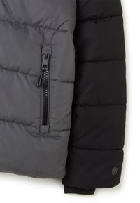 Chaqueta acolchada con un diseño en bloques de color gris y negro, con costuras horizontales, un bolsillo con cremallera y un logotipo en la manga.