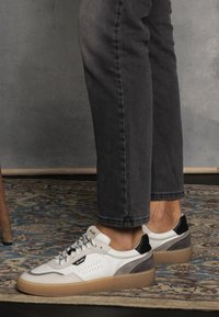 Sneaker bianche in pelle con accenti grigi e neri, caratterizzate da una finitura testurizzata, punta rotonda e lacci a contrasto. Suola in gomma con un leggero plateau.