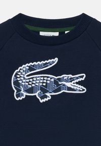 Felpa blu navy con logo ricamato di un coccodrillo bianco e blu, caratterizzato da motivi geometrici, collo rotondo e polsini a costine.