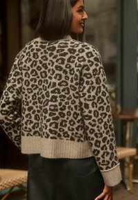Grauer Pullover mit schwarzem Leopardenmuster, geripptem Saum und Bündchen, verkürztem Design, weichem Textil, getragen über einem schwarzen, enganliegenden Unterteil.