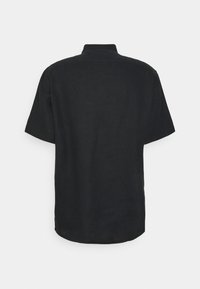 Chemise noire à manches courtes avec un ourlet droit et un col, vue de dos sur un fond gris clair uni.