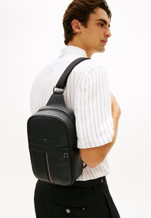 Svart skinnryggsekk med glidelåslukking, med en stripete detalj. Kompakt design med justerbar stropp og strukturert materiale.