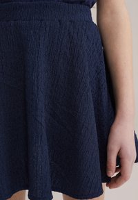 Marinblå kjol i strukturerad tyg med en utsvängd design. Har en rynkad midja och når till mitten av låret.