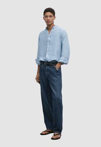 Light blue linen shirt with button front, rolled sleeves, dark blue denim jeans, and black flip-flops. Simple, casual outfit.