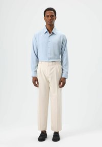 Light blue button-up shirt with long sleeves and a soft texture, paired with high-waisted, cream-colored trousers and black shoes.