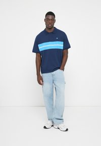 Marinblå pikétröja med ett ljusblått horisontellt rand, korta ärmar och krage. Buren med ljusblå jeans och vita sneakers.