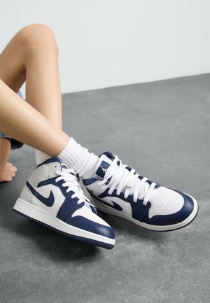 Le sneakers alte in pelle bianche e blu navy presentano una punta perforata, una suola spessa e lacci bianchi, abbinate a calzini corti bianchi a coste.