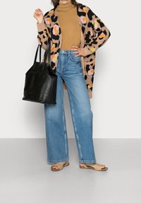 Kardigan w panterkę w kolorach brązowym, różowym i żółtym, noszony na beżowym golfie, zestawiony z wysokim stanem niebieskich dżinsów i czarną torbą na ramię.