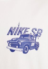 Bílý tričko s modrou grafikou vintage kamionu, na němž je nahoře text "NIKE.SB" a k zadní části kamionu je připojena tažná linie.