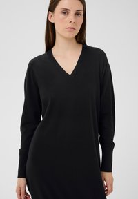 Schwarzes V-Ausschnitt-Kleid mit langen Ärmeln, hergestellt aus einem glatten, leichten Strickstoff. Es zeichnet sich durch eine lockere Passform und gerippte Bündchen aus.