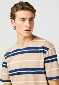 Camiseta de algodón beige con rayas horizontales en azul marino y blanco. Presenta un cuello redondo y mangas cortas. Diseño suave y casual.