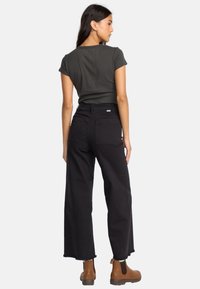 Black wide-leg jeans with frayed hem, high waist, two back pockets, paired with a dark grey fitted t-shirt and brown ankle boots.