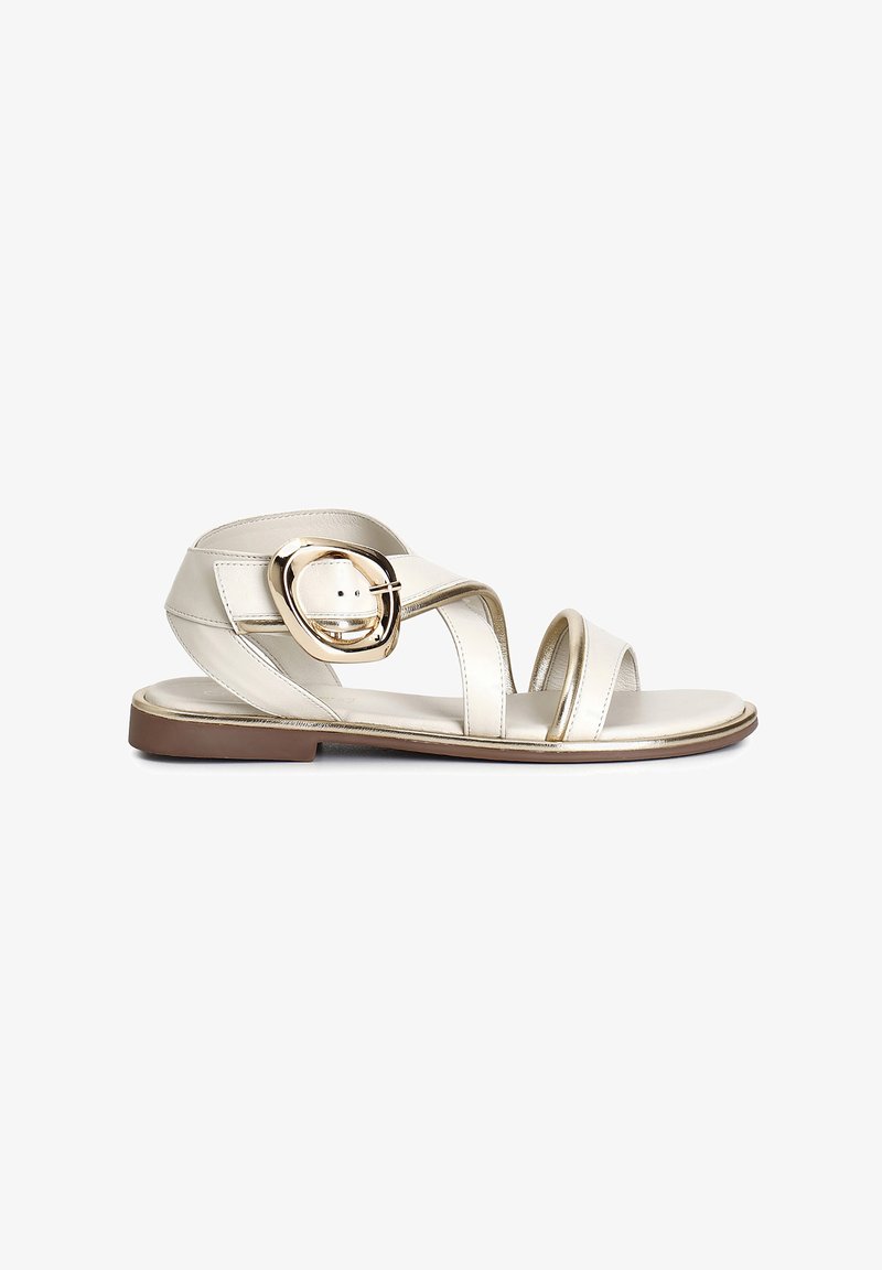 Metallic silver sandals with crisscross straps, a circular buckle accent, flat sole, and a minimalist design. Smooth texture and low profile.