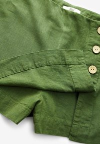 Grön linnaskjorta med en texturerad yta, som har överdimensionerade knappar och en lätt draperad design. Kragen är mjuk och utvidgad.