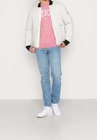 Vit pufferjacka med svarta ärmslut, rosa sweatshirt med Nike-logotyp, ljusblå jeans och vita sneakers. Enkel, avslappnad outfit.