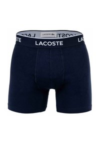 Tengerészkék pamut boxeralsó fehér Lacoste logós derékszíjjal. Kényelmes illeszkedéssel és combközép hosszúságú kialakítással rendelkezik, megerősített varrásokkal.