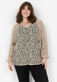 Bluse med blonde og sort blomstermønster, beige baggrund, V-hals og gennemsigtige ballonærmer. Stylet med sorte bukser.