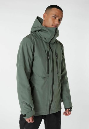 Giacca impermeabile verde con colletto alto, zip anteriore e molteplici tasche con zip. Presenta una texture liscia e polsini regolabili.