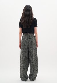 Pantaloni a gamba larga realizzati in tessuto houndstooth testurizzato nei toni del nero, grigio e multicolore, con una cintura scura, abbinati a una maglietta nera aderente.