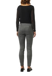 Czarna bluzka z długim rękawem i okrągłym dekoltem, zestawiona z szarymi spodniami w kratę do kostek oraz czarnymi butami wsuwanymi. Gładki materiał i dopasowany krój.