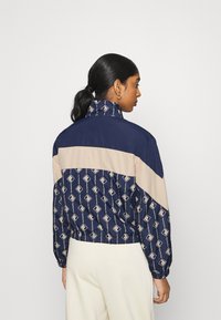 Giacca a vento blu navy e beige con motivo stampato geometrico, colletto alto, polsini elasticizzati e una vestibilità corta.