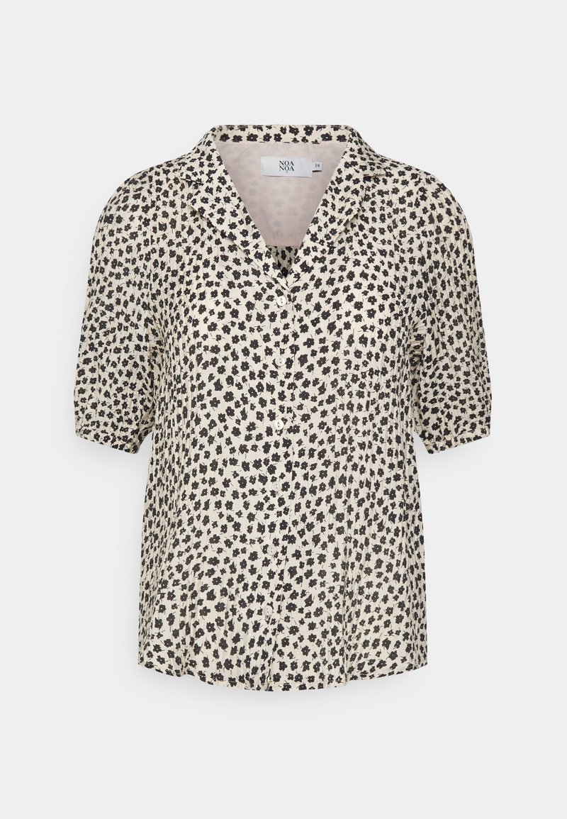 Blusa a maniche corte di un beige chiaro con un motivo floreale nero. Presenta un colletto e una chiusura a bottoni, realizzata in un tessuto leggero.