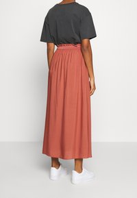 Maxi nederdel i rustfarve med samlet talje, parret med en løse pasform i kulfarvet t-shirt og hvide sneakers. Glat stof.