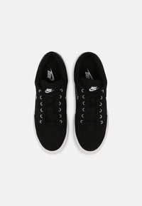 Svarta kanvas sneakers med vita gummisålar, utrustade med silverfärgade öglor och snörningar, med en logotyp på tungan och sidan.