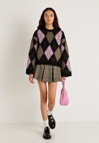 Μπλούζα με ασπρόμαυρο και ροζ ρόμβο και υπερμεγέθη μανίκια, σε συνδυασμό με πλισέ καρό φούστα. Αξεσουάρ: ροζ τσάντα και μαύρα παπούτσια.