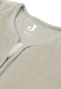 Vêtement en tissu beige clair avec une texture douce et chaleureuse, doté d'un simple col en V, portant une étiquette de taille indiquant "70 cm".