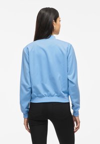 Hele sinine bomber-jakk, mis on valmistatud siledast kangast, ribitud alläärte ja mansettidega, varustatud püsti krae ja sobiva lõikega.