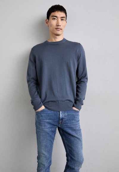 Navy knitted sweater with crew neck and ribbed cuffs, paired with light blue jeans. The material appears soft with a smooth texture.