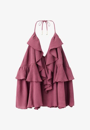 Donna che indossa un top viola senza maniche con balze, shorts in denim neri e sandali marroni con borchie, in piedi davanti a uno sfondo bianco neutro.