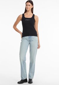 Black tank top with logo, fitted design, round neckline, paired with light blue straight-leg jeans and black ankle boots.