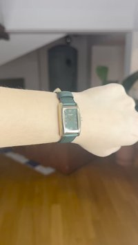 Ristkülikukujuline kell rohelise nahkrihmaga. Kellaplaat on tumeroheline kuldsete detailidega, millel on tunde näitavad märgid ja kuupäeva kuva.