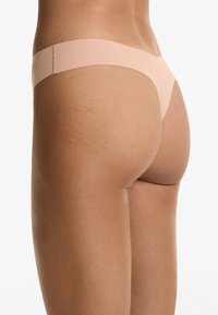 Huidkleurige tanga ondergoed met een gladde, elastische band. Het ontwerp heeft een minimalistische bedekking en naadloze randen voor een gestroomlijnd uiterlijk.