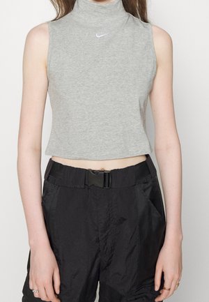 Szary krótki top bez rękawów z białym logo Nike, noszony z czarnymi spodniami z wysokim stanem, z czarnym paskiem i plastikową klamrą.