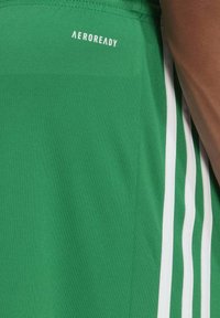 Green athletic shorts with white stripes, made of breathable fabric. Features “AEROREADY” logo on the waistband. Smooth texture.