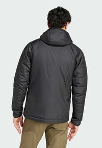 Zwarte pufferjack met hoge kraag en aangehechte capuchon. Kenmerkt zich door een doorgestikte textuur en aansluitende mouwen, ontworpen voor warmte en comfort.