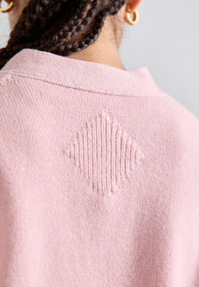 Roze gebreide trui met een ronde kraag, voorzien van een ruitvormig textuurdetail op de achterkant. Zachte textuur en gelijkmatig breipatroon.