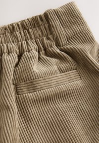 Pantaloni taupe din catifea cu suprafață texturată, cu nervuri, cu talie elastică și un buzunar posterior singular cu detaliu de cusătură orizontală.