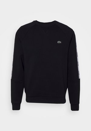 Sudadera negra con mangas raglán, presenta un logo bordado en verde y rayas laterales blancas con texto. Tejido suave y puños acanalados.