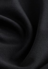 Gros plan sur un tissu tricoté noir et doux avec une fine texture côtelée visible et des plis doux créant des ombres à la surface.