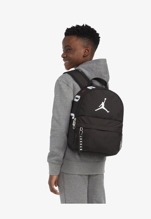 Mochila negra con logo blanco, con forma redondeada, bolsillo delantero con cremallera, etiquetas de acento y bolsillo lateral de malla.