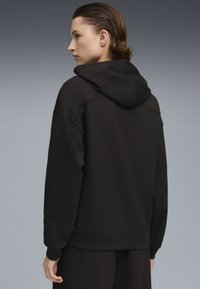 Sort hætte sweatshirt med kengurulomme, afslappet pasform, ribbede manchetter og kant, samt et blødt, tekstureret stof. Hætten er fastgjort ved halsudskæringen.