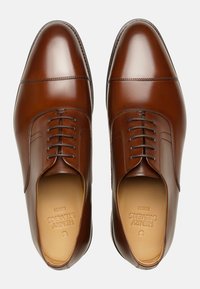 Bruine leren dresschoenen met een gepolijste afwerking, ronde neus en vetersluiting. Voorzien van ton-sur-ton stiksels en een gladde binnenvoering.